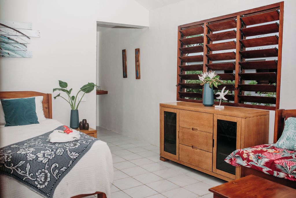 Un dormitorio con cama, un armario de madera, una planta en maceta y un panel decorativo en la pared.