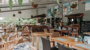An indoor restaurant with wooden tables and chairs, hanging plants, and a beach-themed wall.
