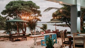 An outdoor seating area with tables and chairs, surrounded by trees and overlooking the ocean.
