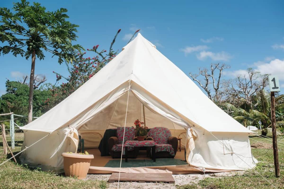 A large white tent with a sofa and chairs inside, surrounded by trees and a clear sky.