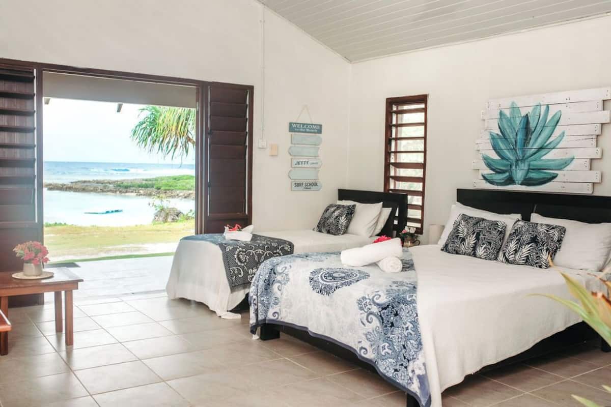A hotel room with two beds, a view of the ocean, a surf school sign, and a welcome sign.