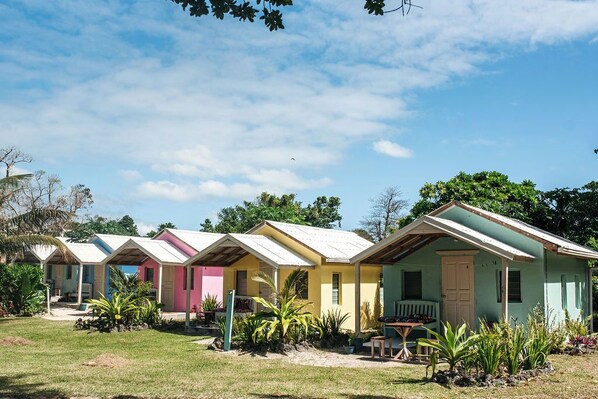 A row of colorful, single-story cabins with a grassy yard and tropical plants. - Le Life Resort (Epule)