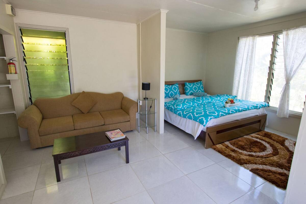 A room with a sofa, a bed with patterned bedding, a small table, and a rug.
