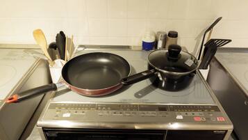 A kitchen with a stove, a frying pan, a pot, and various utensils.