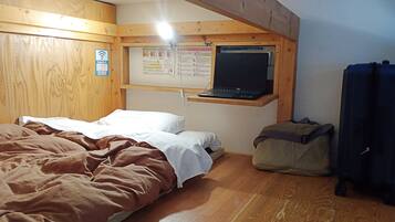 A room with a bed, a desk with a laptop, a bulletin board, and a bag.