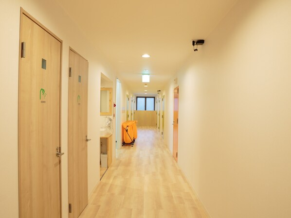 A hotel hallway with wooden doors, a shower area, and a camera on the ceiling.