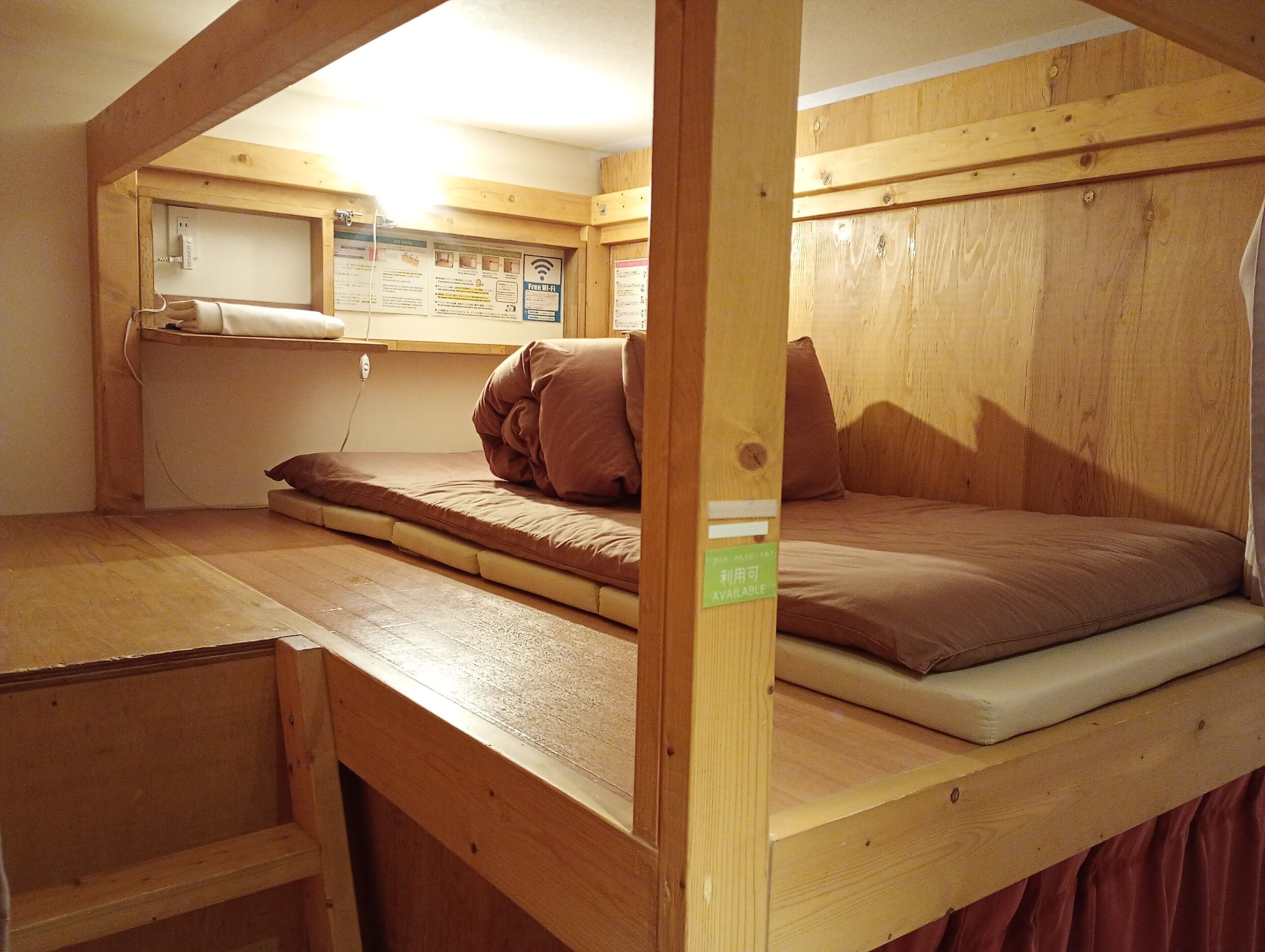 A small, wooden, single-bed room with a bunk bed and a desk area.