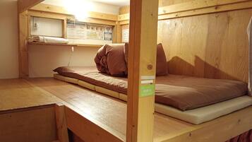 A small, wooden, single-bed room with a bunk bed and a desk area.