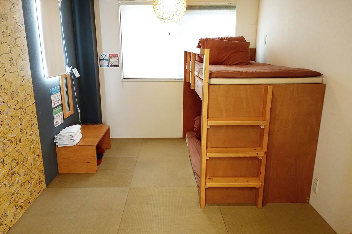 Una habitación pequeña y funcional con una cama litera, un escritorio de madera y una ventana con persianas.