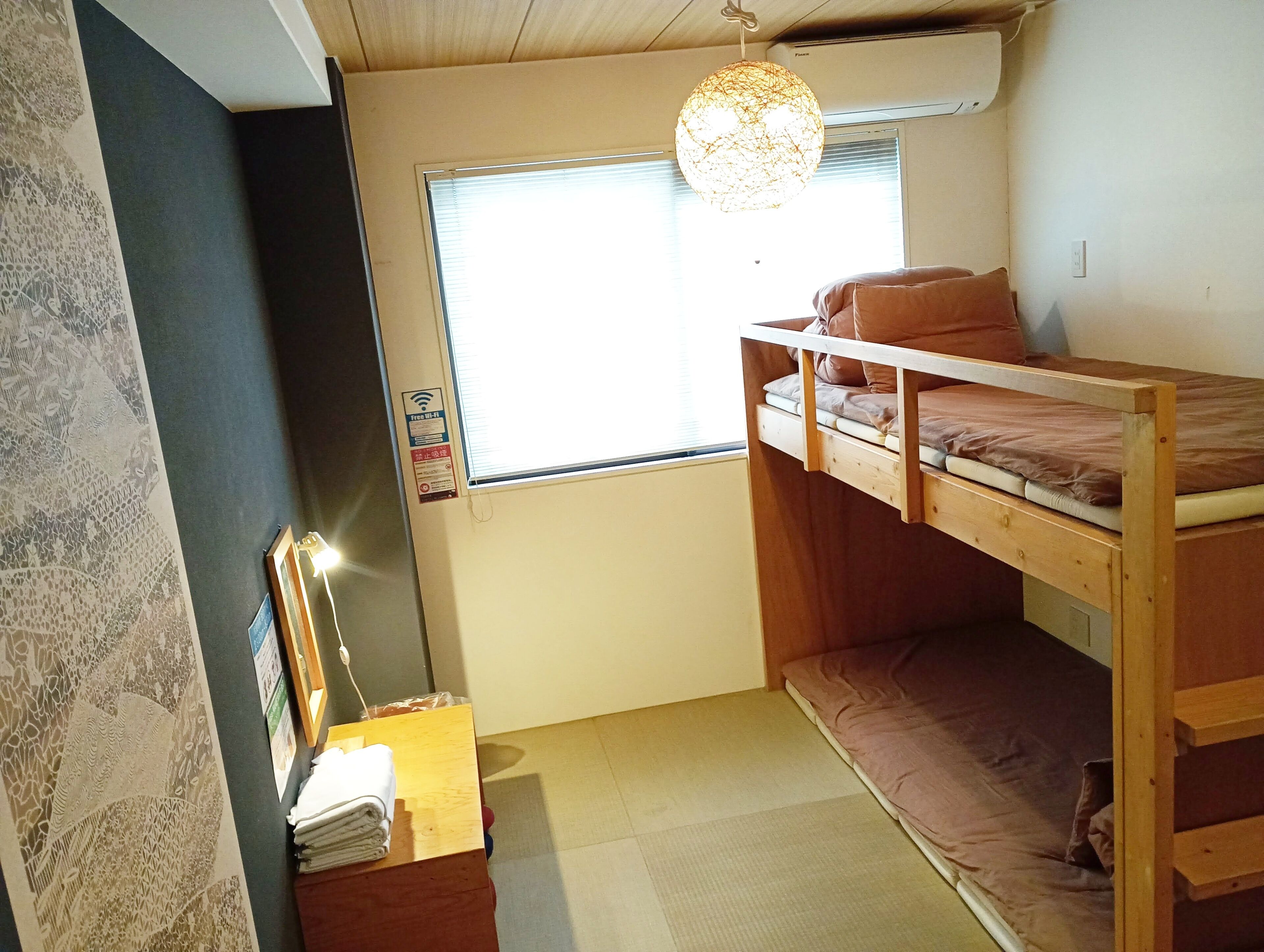 Una habitación pequeña con una cama litera, un escritorio con lámpara, una ventana con persianas y un elemento decorativo en la pared.