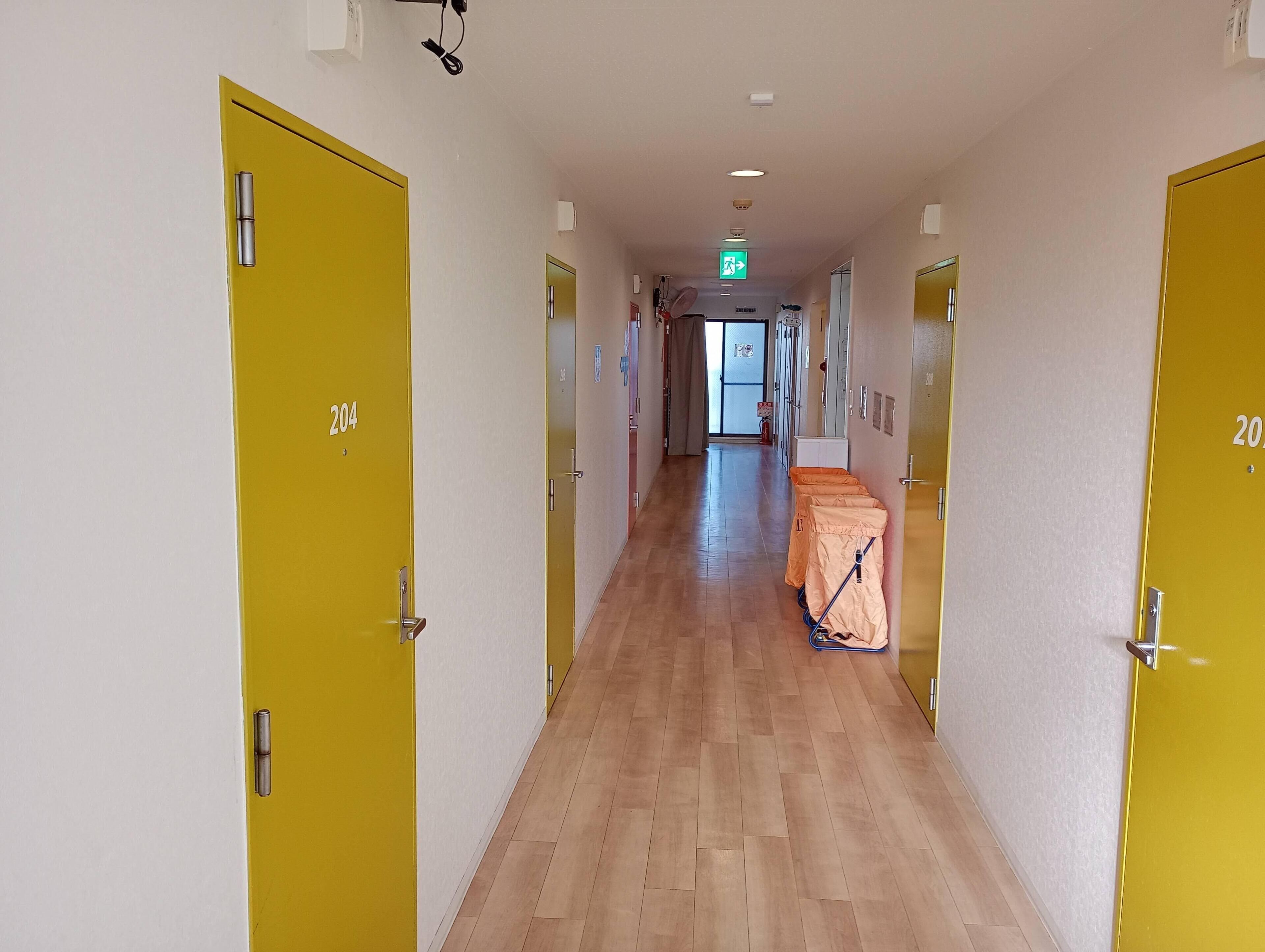 Een hotelgang met gele deuren, genummerd 204 en 205, houten vloer en een zichtbare brandblusser.