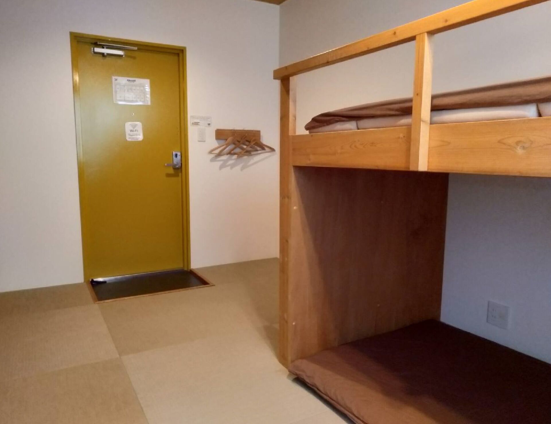 A room with a bunk bed, a yellow door with a Wi-Fi sign, and a small shelf with folded clothes.
