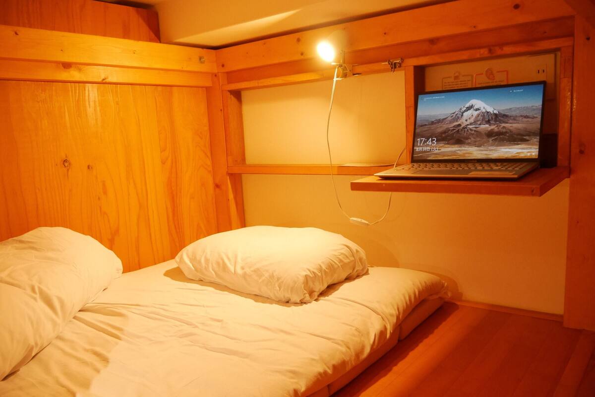 Habitación de cabaña de madera con una cama, una laptop montada mostrando un paisaje montañoso y una repisa en la pared.
