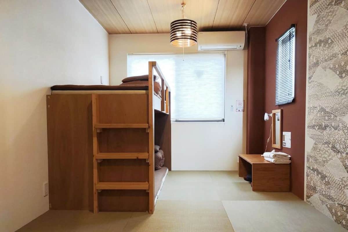 Una habitación con literas, un escritorio pequeño, un espejo y una ventana con persianas.