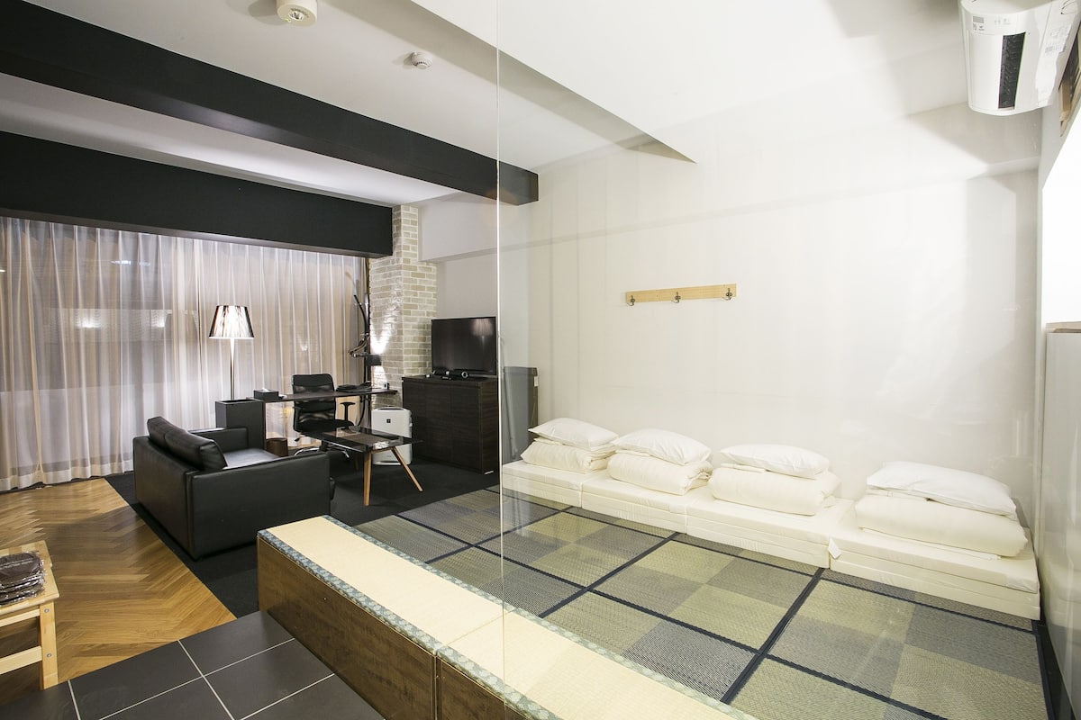 A modern hotel room with a sofa, a small desk, a bed with pillows, and a glass partition.