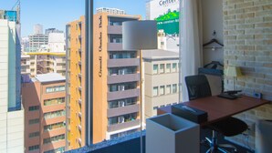 A modern office space with a view of high-rise buildings, a desk, office chair, and a lamp.