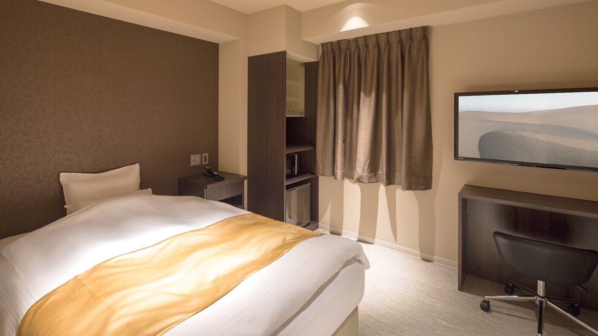 A hotel room with a bed, a desk, a chair, a television, and a wardrobe.