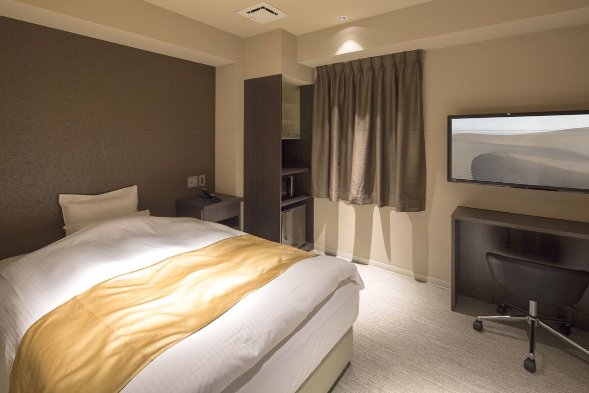 Une chambre d’hôtel dotée d’un grand lit, d’un téléviseur à écran plat fixé au mur, d’un bureau avec une chaise et d’une bibliothèque intégrée.