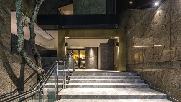 A modern building entrance with marble steps, a glass railing, and a stone wall.