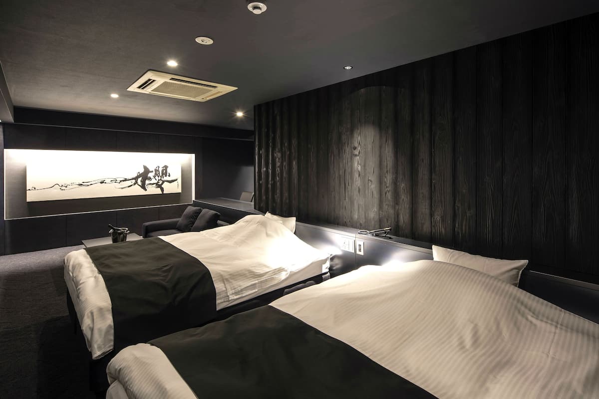 Une chambre d’hôtel moderne avec deux lits, un grand téléviseur fixé au mur et un mur revêtu de panneaux en bois foncé.