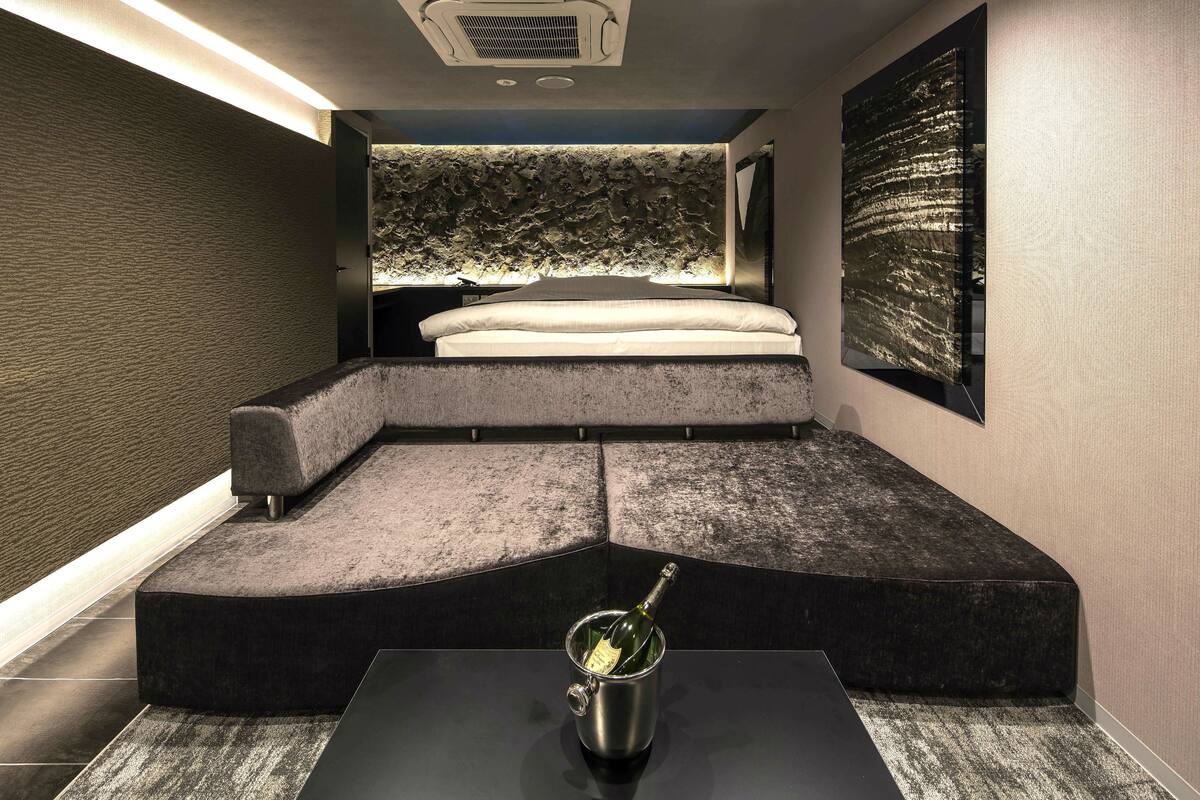 Une chambre moderne avec un lit aux lignes courbes, un petit coin salon et une bouteille de champagne posée sur une table.