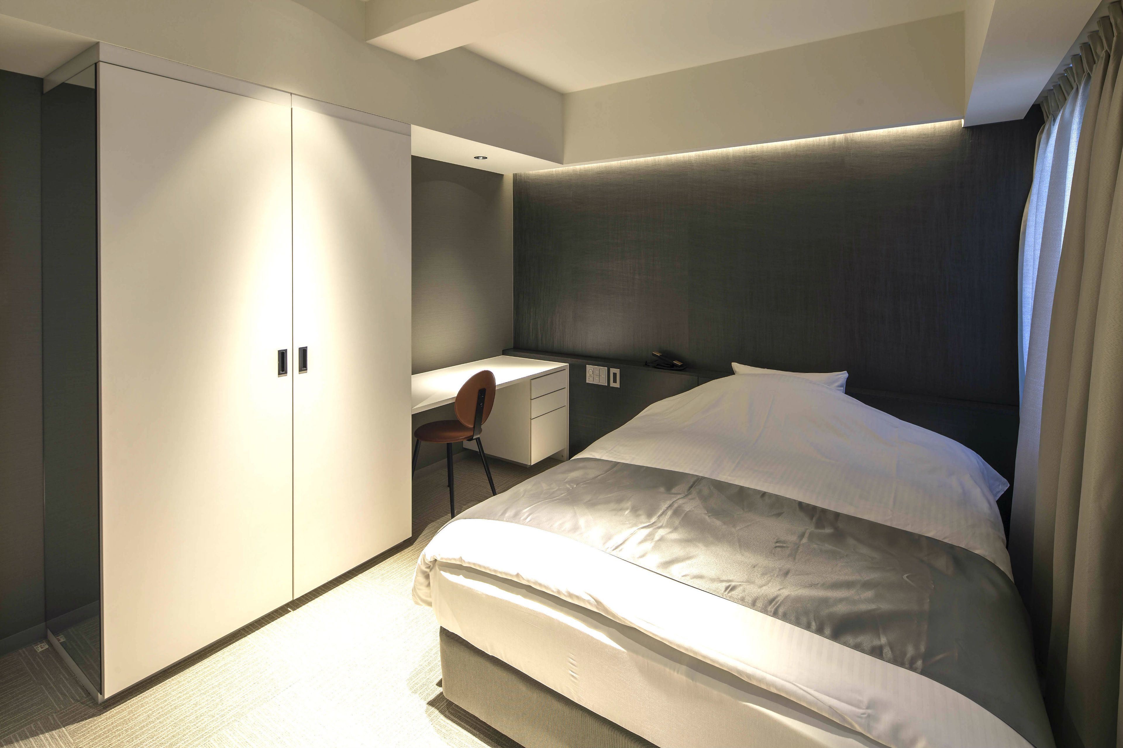 A modern hotel room with a large bed, a desk, and a wardrobe.