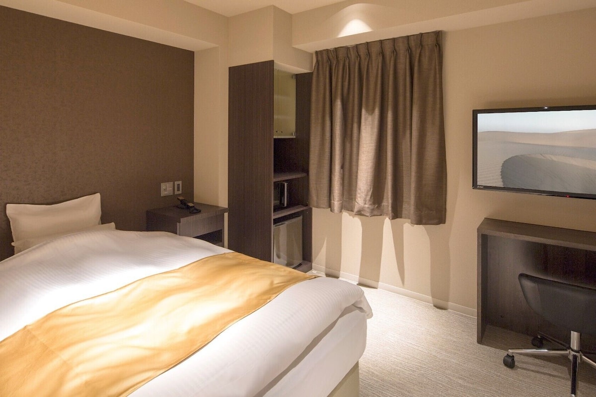 Une chambre d’hôtel équipée d’un lit, d’un bureau, d’une chaise, d’une télévision et d’une armoire.