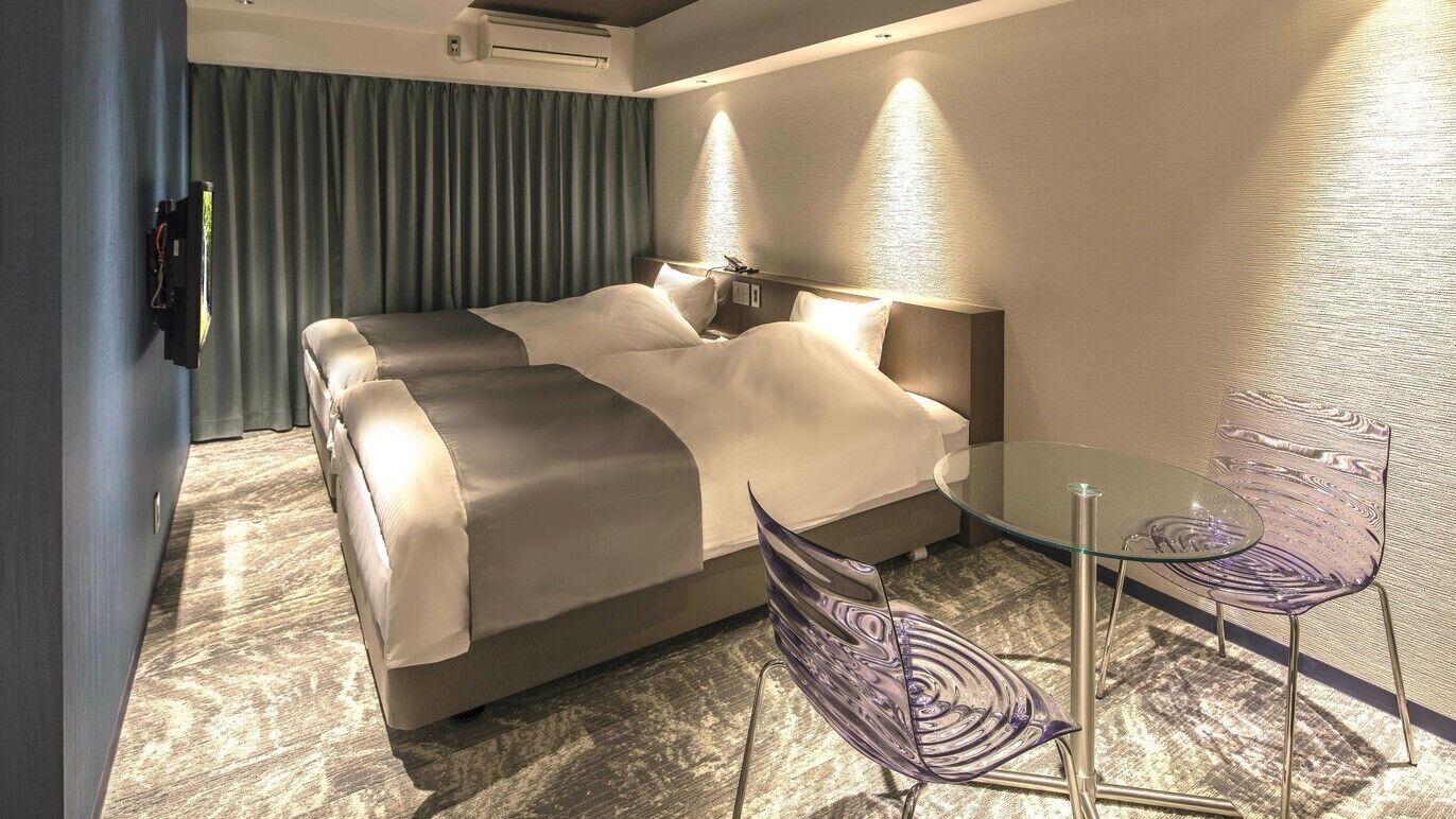 A modern hotel room with a bed, bedside table, and a glass table with chairs.