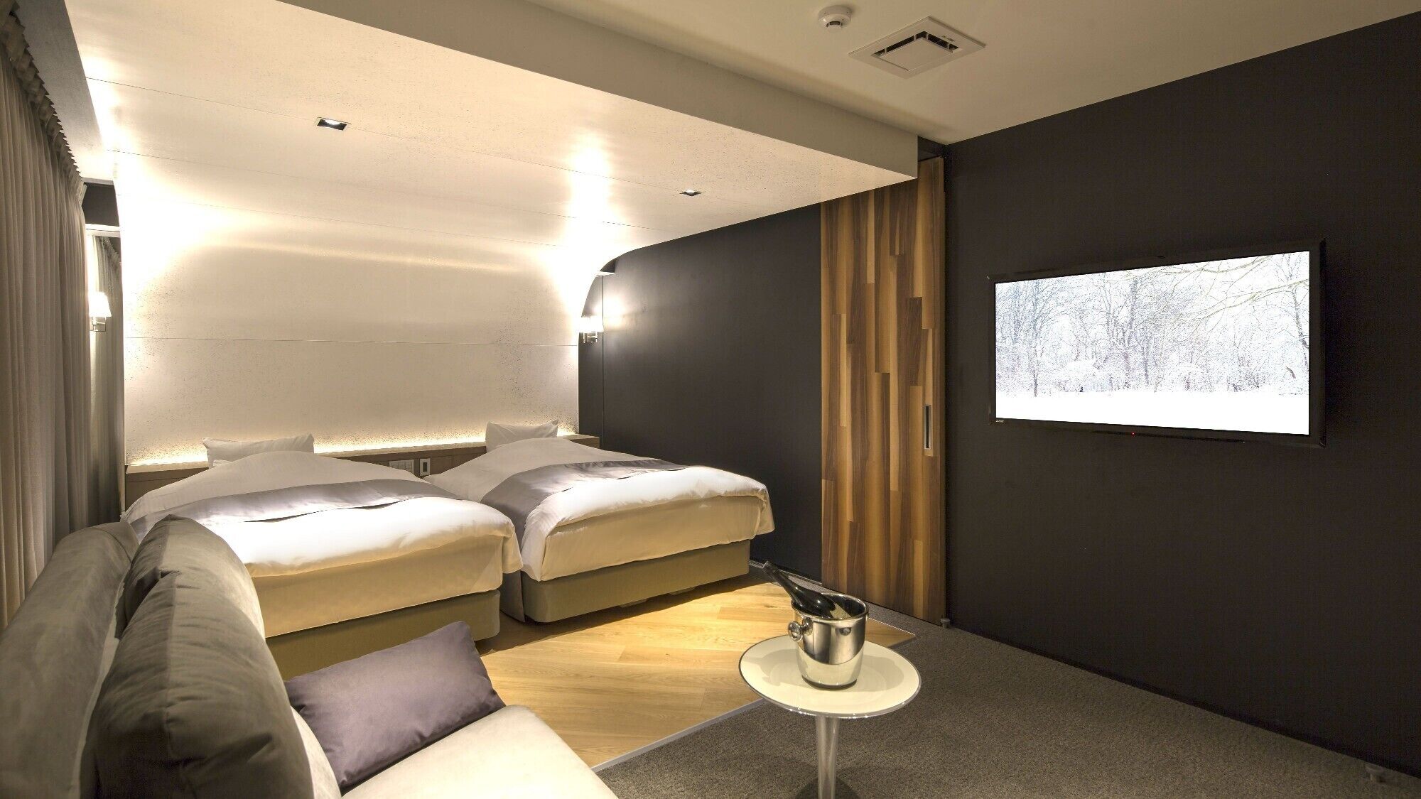 Una habitación de hotel moderna con dos camas, una mesita y una televisión que muestra un paisaje nevado.