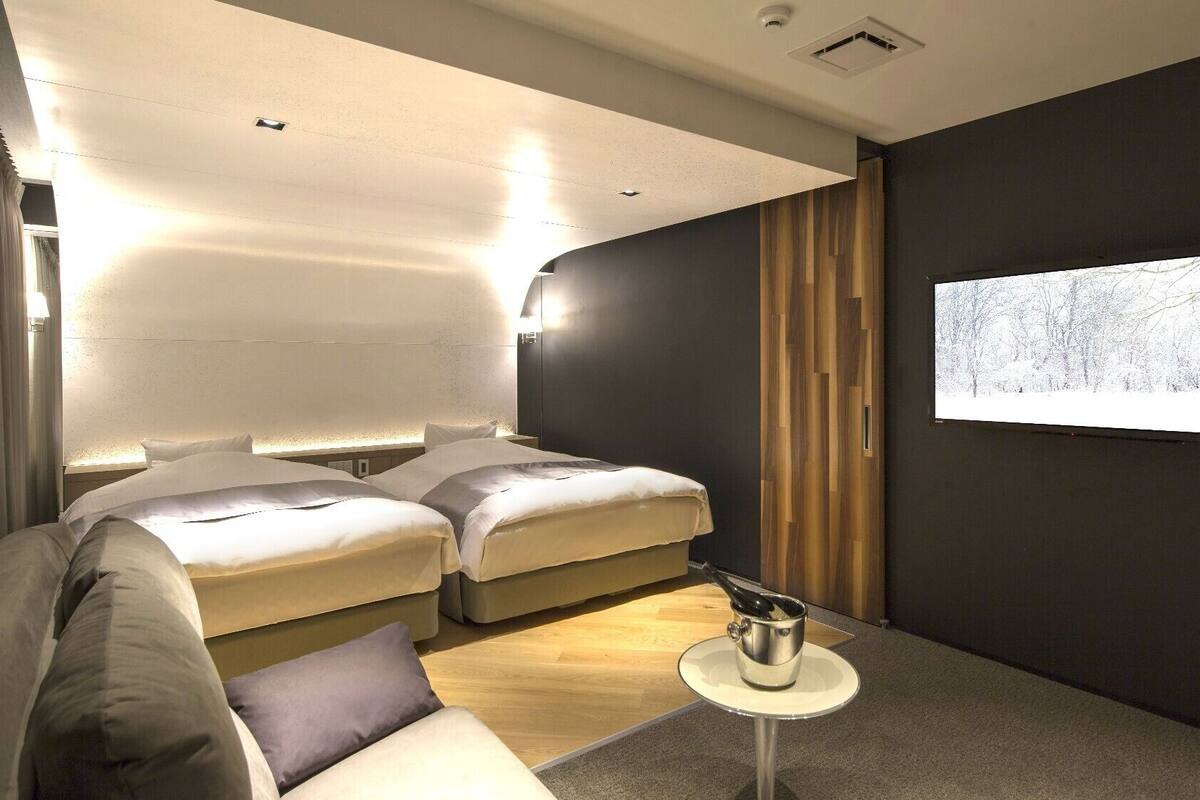 Une chambre d’hôtel moderne avec deux lits, une petite table et un écran de télévision diffusant un paysage enneigé.