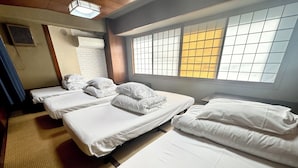 A hotel room with three neatly made beds, a large window with a view, and a traditional Japanese-style sliding door.