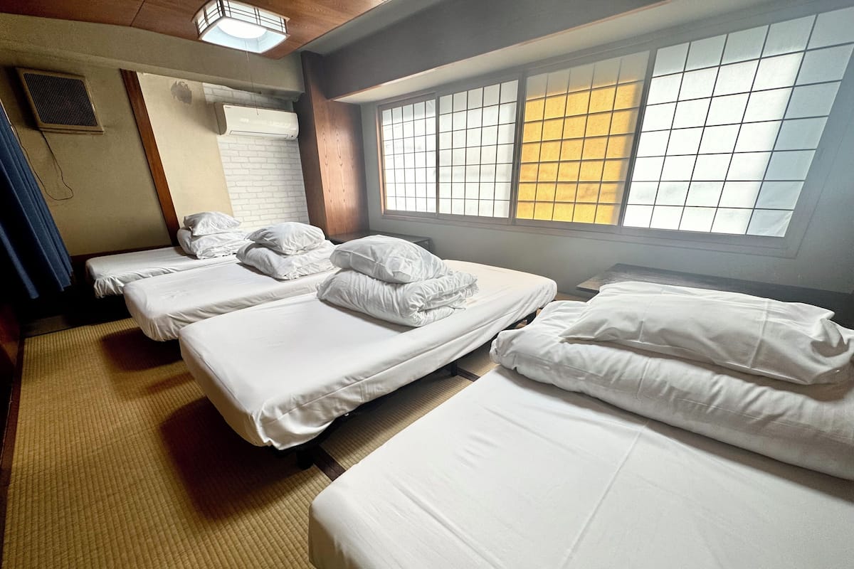 A hotel room with three neatly made beds, a large window with a view, and a traditional Japanese-style sliding door.
