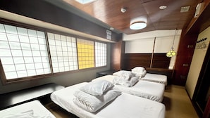 A hotel room with three beds, a wooden ceiling, and a large window with a grid pattern.