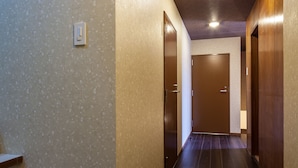 A hallway with wooden floors, a staircase on the left, and doors on both sides leading to other rooms.