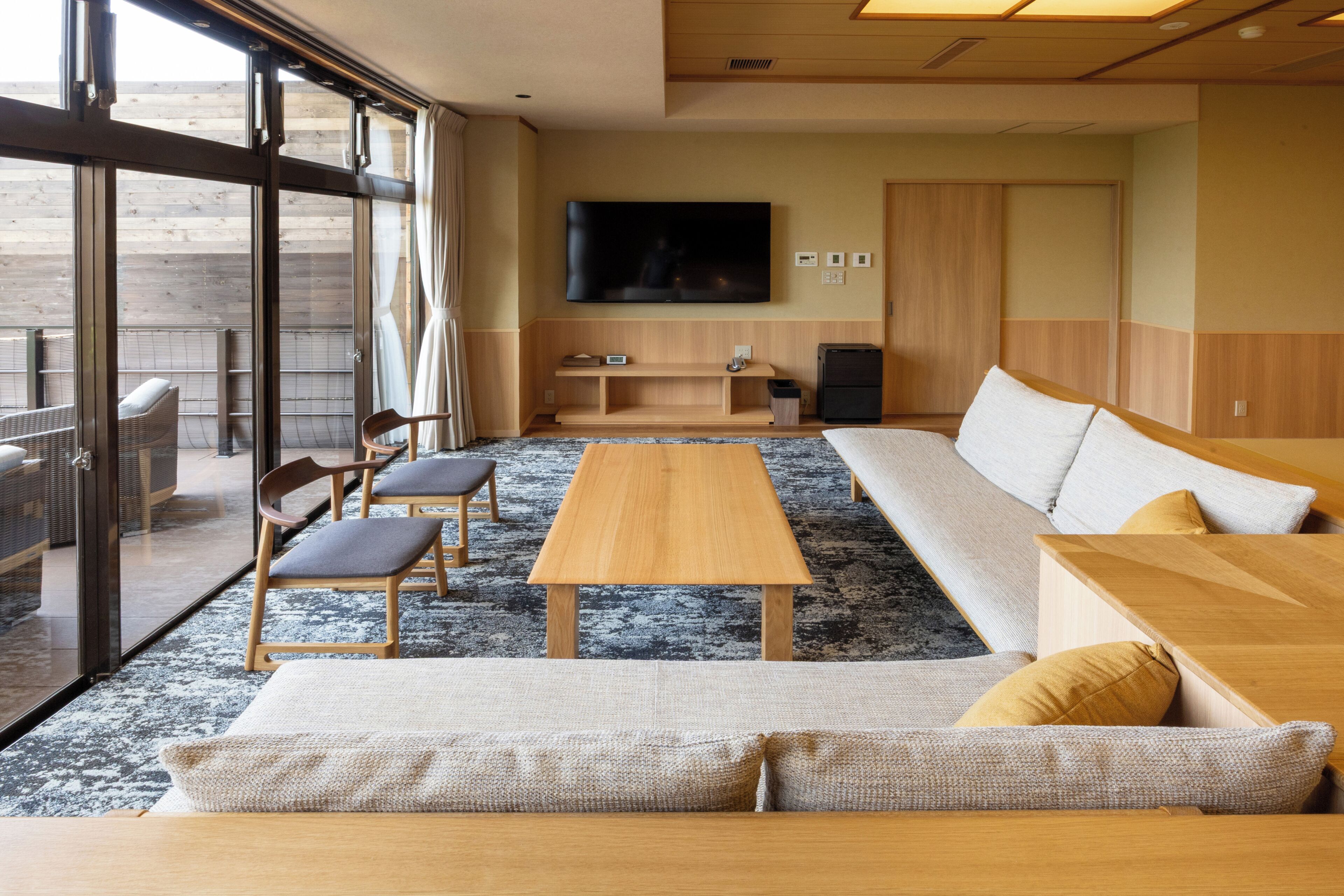 Una sala de estar moderna con sofá, mesa de centro de madera y sillones, un televisor de pantalla plana montado en la pared y un ventanal con vistas.
