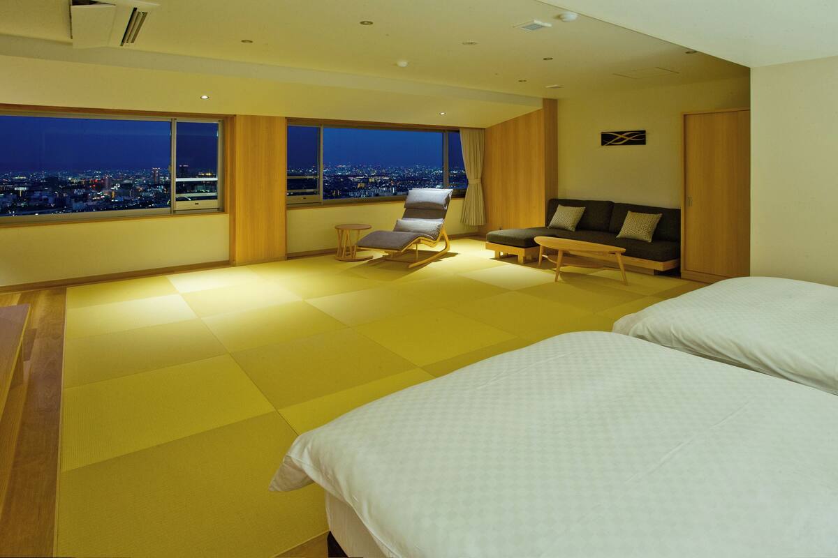 Een hotelkamer met uitzicht op de stad, een bank, een stoel en twee bedden.