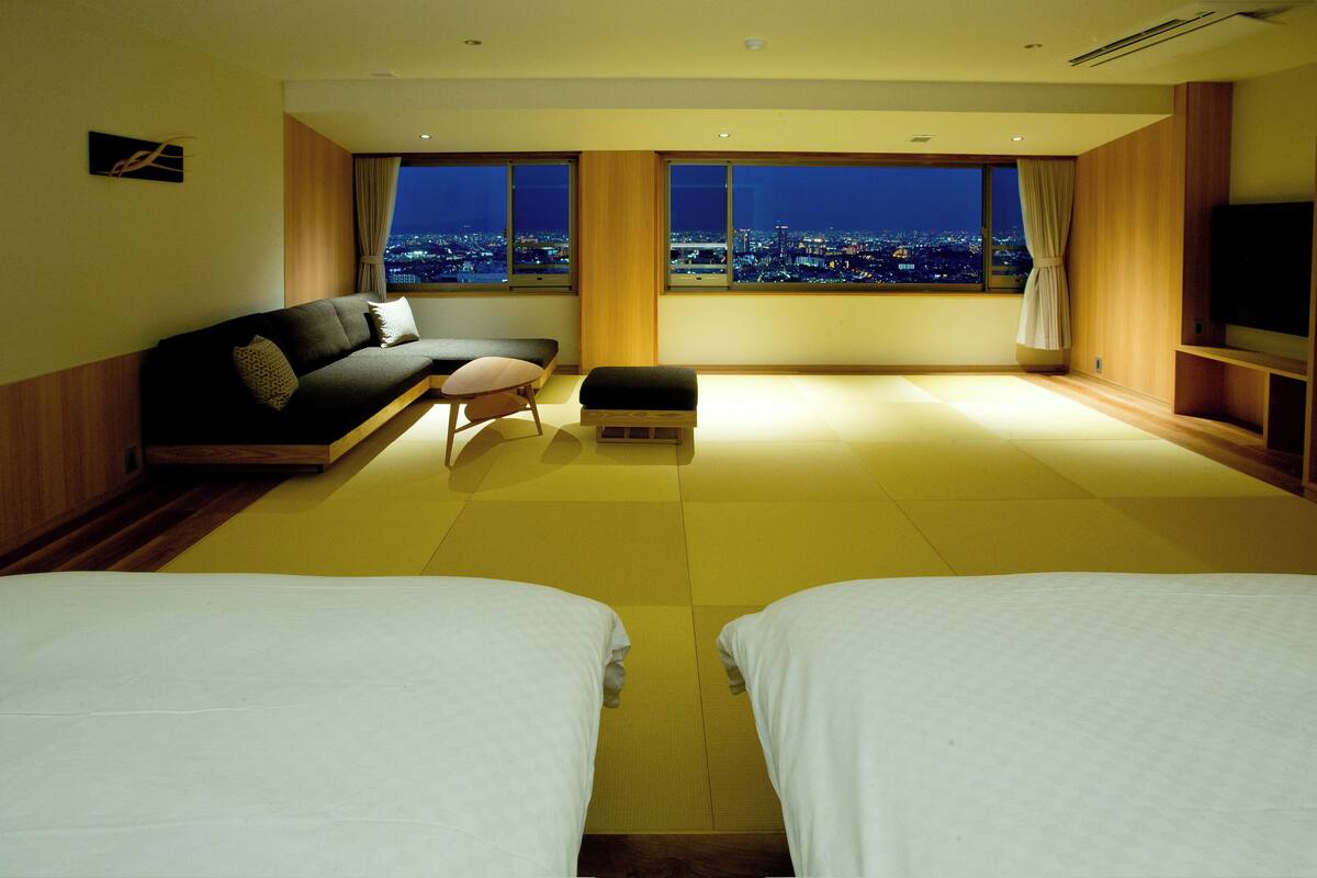 Een hotelkamer met uitzicht over de stad, een bank, een kleine tafel en twee bedden.