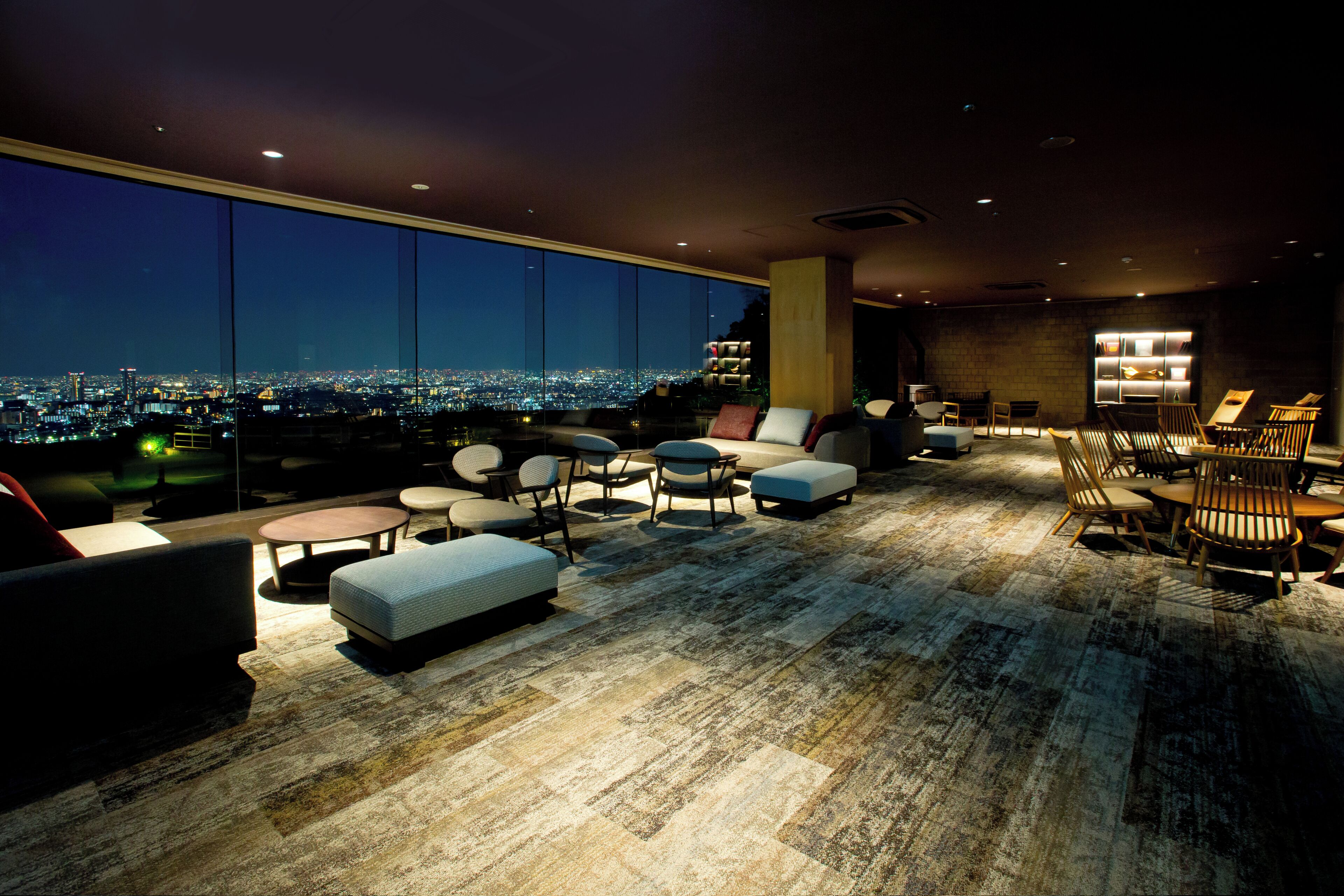 Un salon moderne offrant une vue sur la ville, doté de sièges confortables et d’une grande fenêtre.