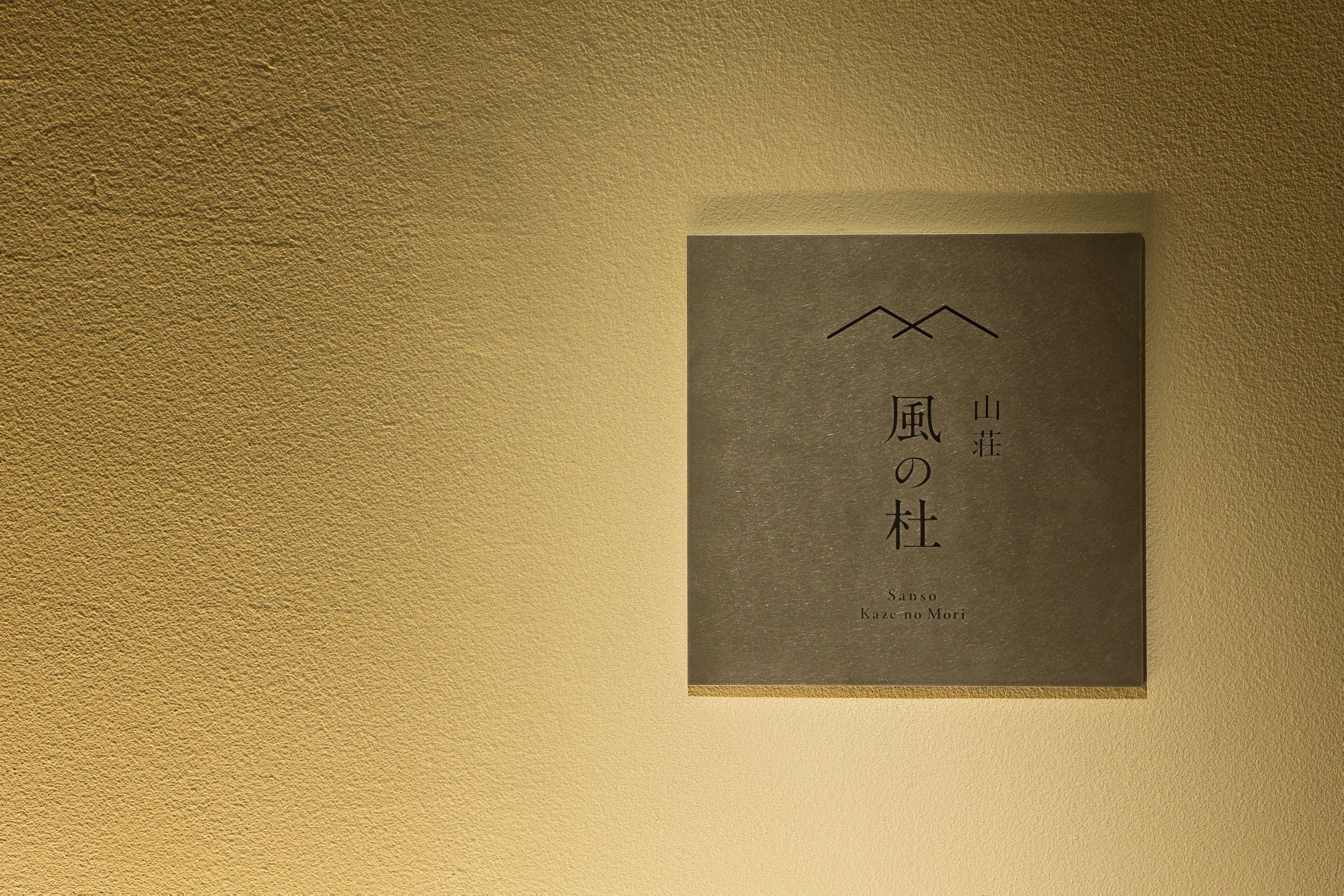 Une plaque encadrée, ornée de caractères japonais et d’un symbole représentant une montagne, fixée à un mur à texture.