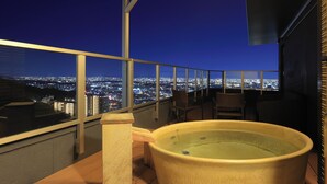 Een balkon met uitzicht op de stad, een jacuzzi en rieten stoelen.