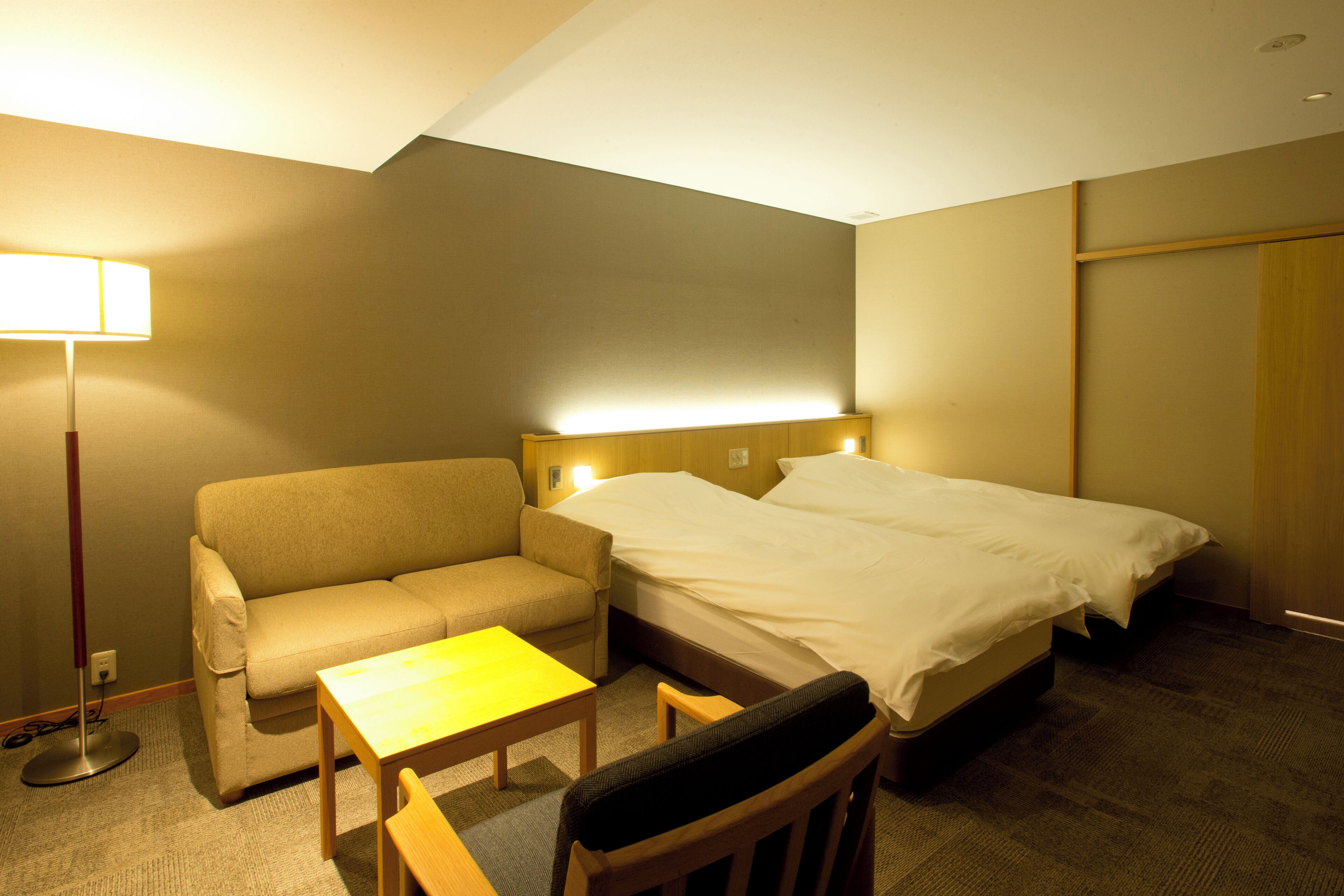 A hotel room with a sofa, a single bed, a small table, and a chair.