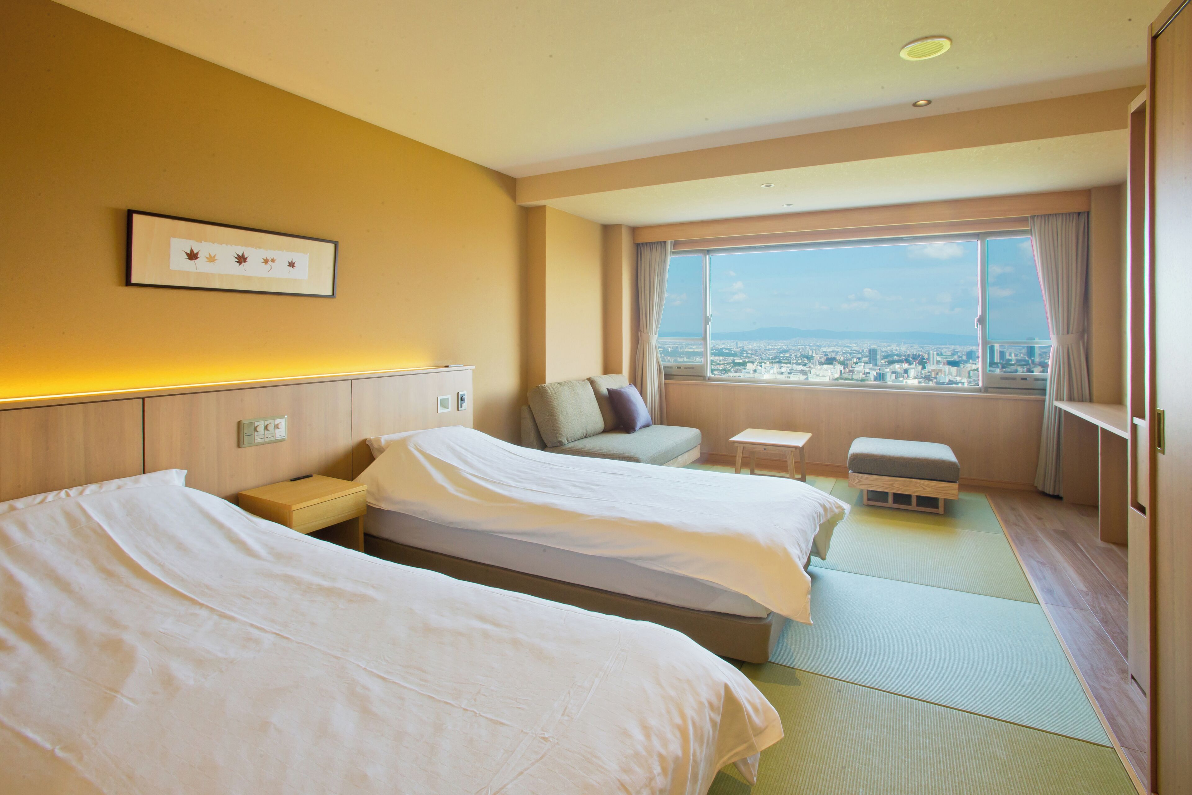 A hotel room with two beds, a small table, a sofa, and a view of the city.