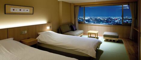 A hotel room with two beds, a sofa, a small table, and a view of a cityscape at night.