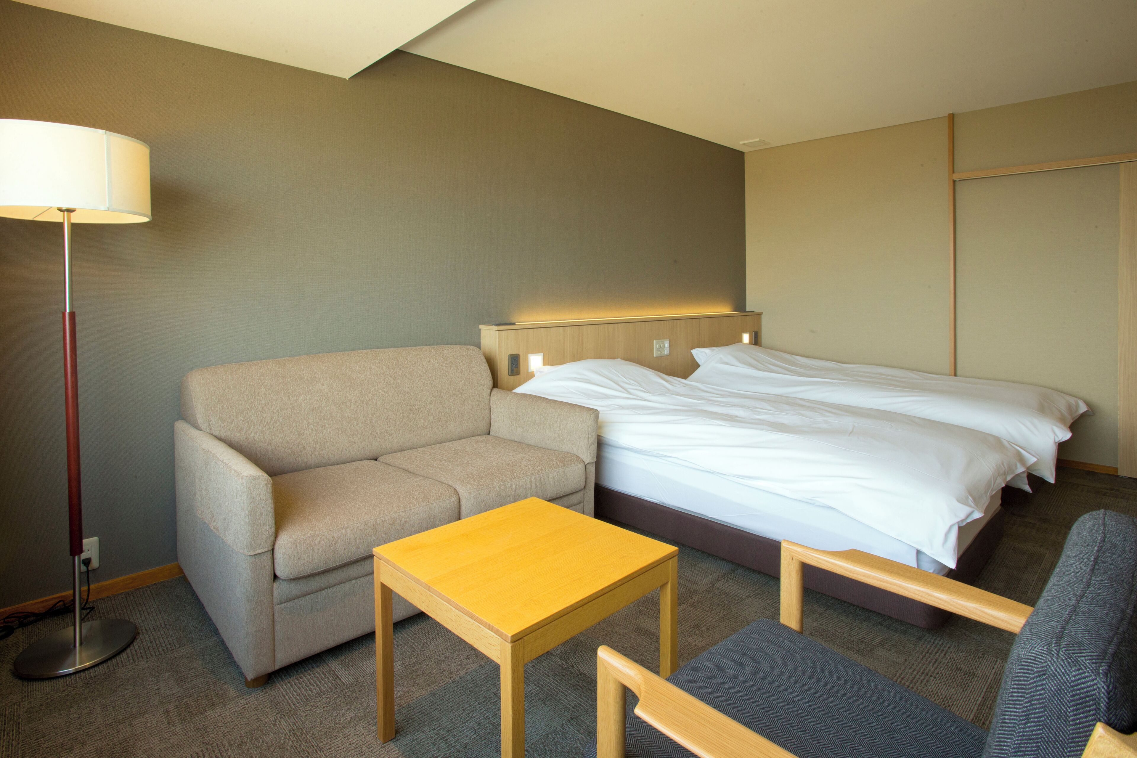 A hotel room with a bed, a sofa, a small table, and a floor lamp.