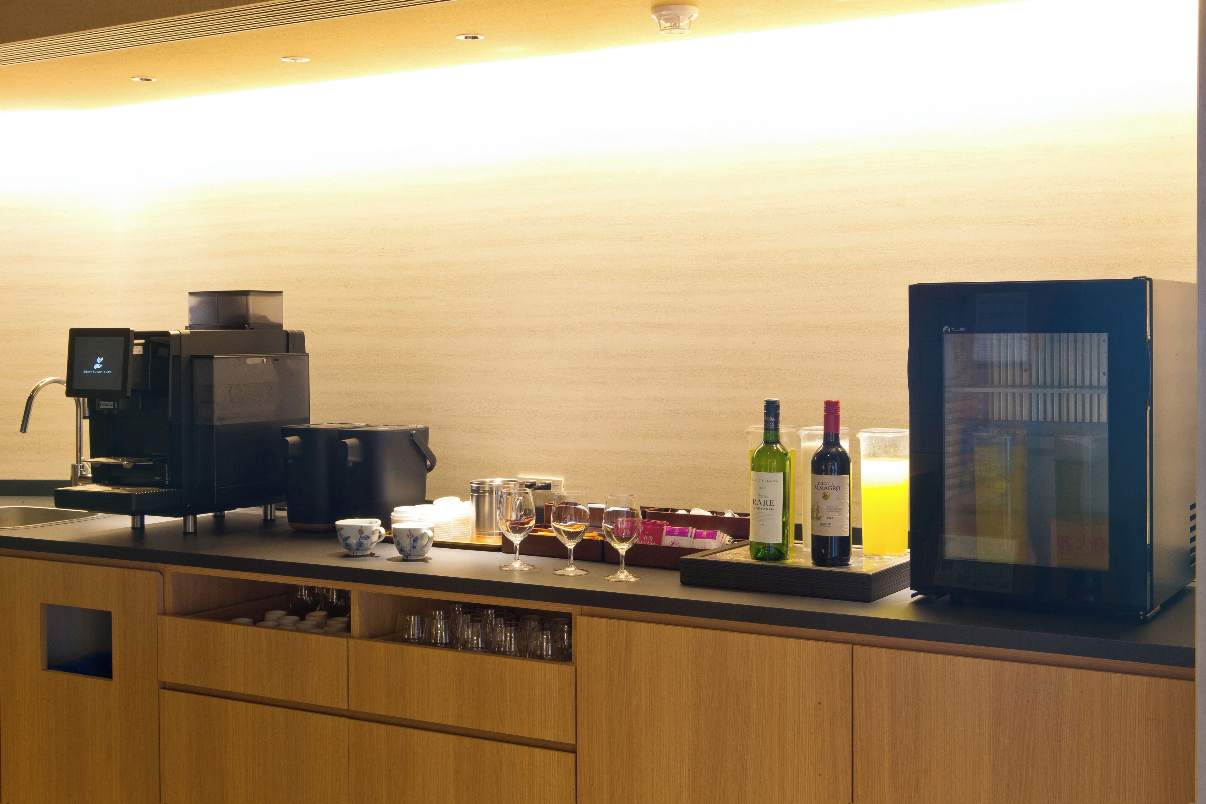 A kitchen area with a coffee machine, wine bottles, and a refrigerator.