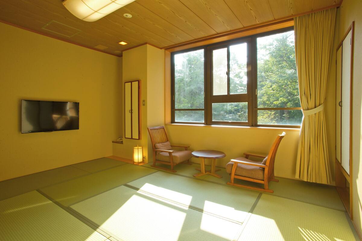 Een kamer met tatami matten, een groot raam, een televisie en traditioneel Japanse meubels.