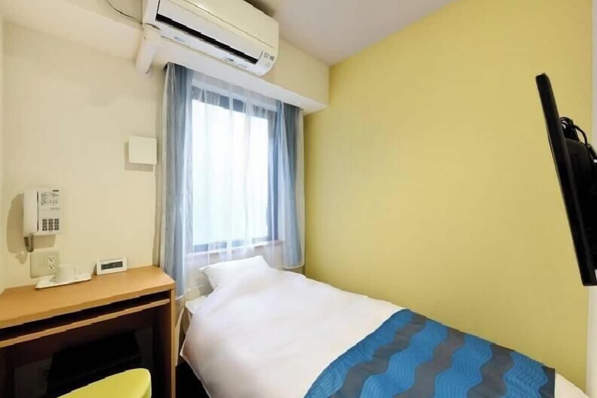 A hotel room with a bed, a desk, a chair, an air conditioning unit, and a window with curtains.