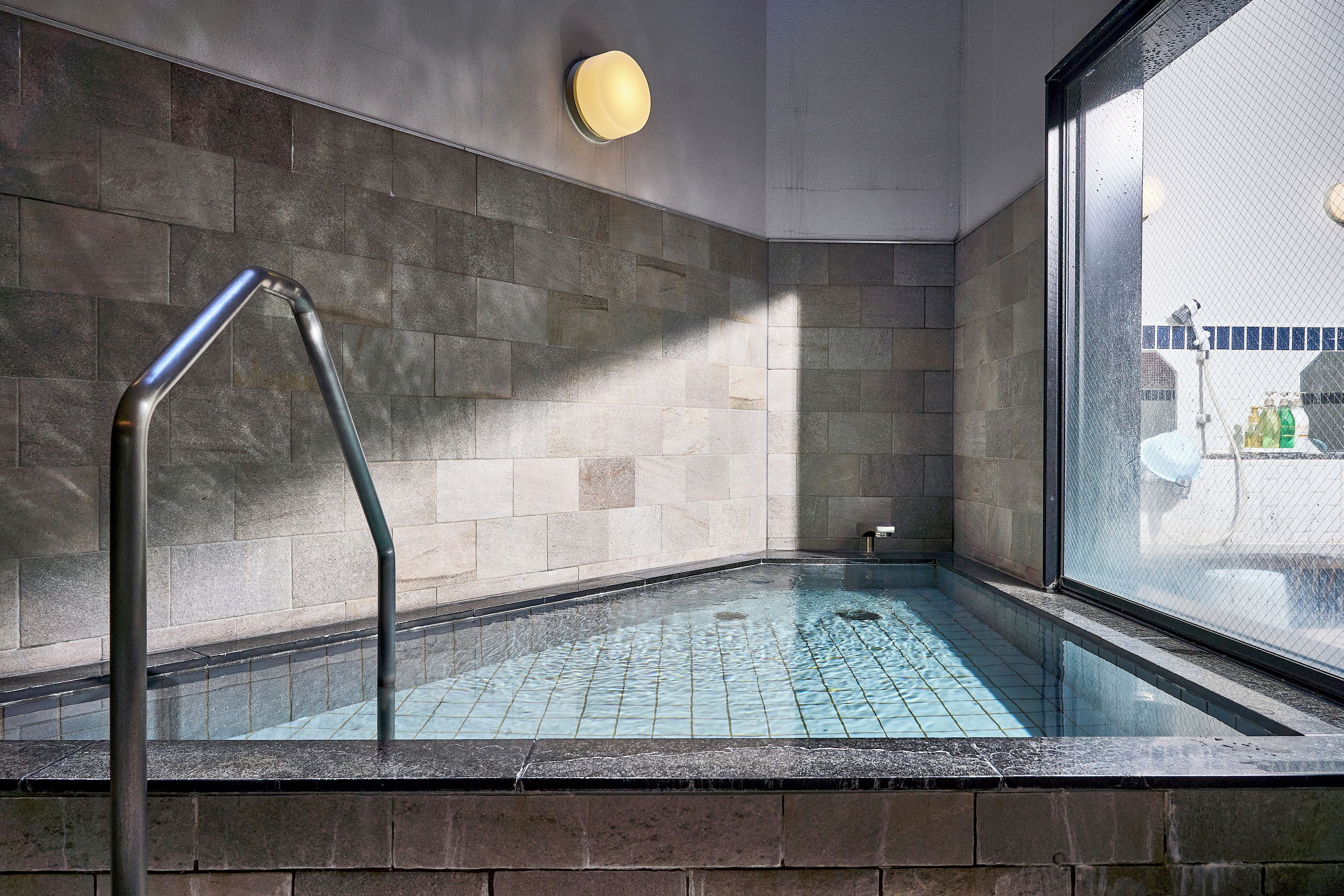 Un área de spa con un jacuzzi envuelto en cristal, un pasamanos de metal y vistas a una piscina exterior.