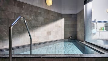 Un área de spa con un jacuzzi envuelto en cristal, un pasamanos de metal y vistas a una piscina exterior.