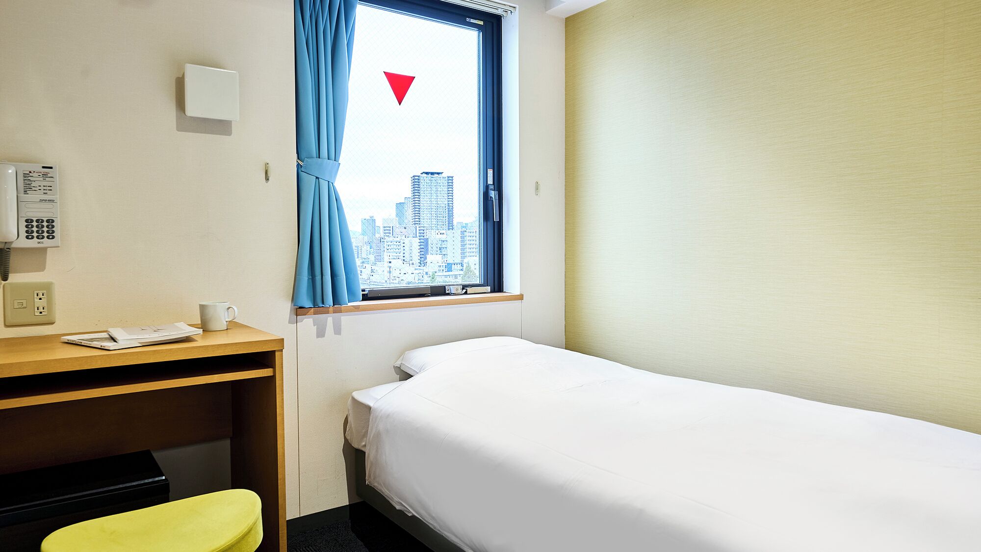 Hotellihuone, jossa on sänky, kirjoituspöytä puhelimineen, tuoli ja ikkuna, josta on näkymä kaupunkiin.